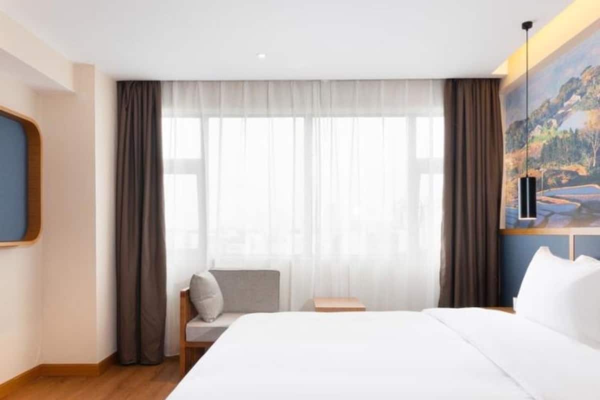 A hotel room with a large bed, a chair, a nightstand, and a painting on the wall.
