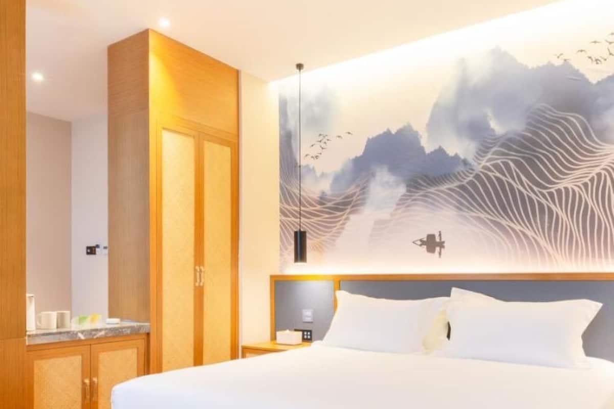 A modern hotel room with a large bed, wooden cabinetry, and a wall-mounted artwork depicting a mountainous landscape.