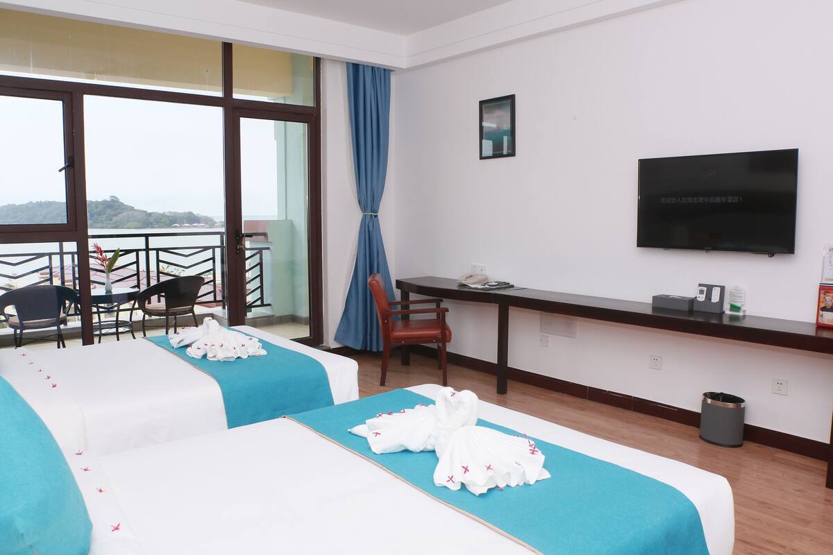 Ein Hotelzimmer mit zwei Betten, einem Schreibtisch, einem Sessel, einem Fernseher und einem Balkon mit Blick.