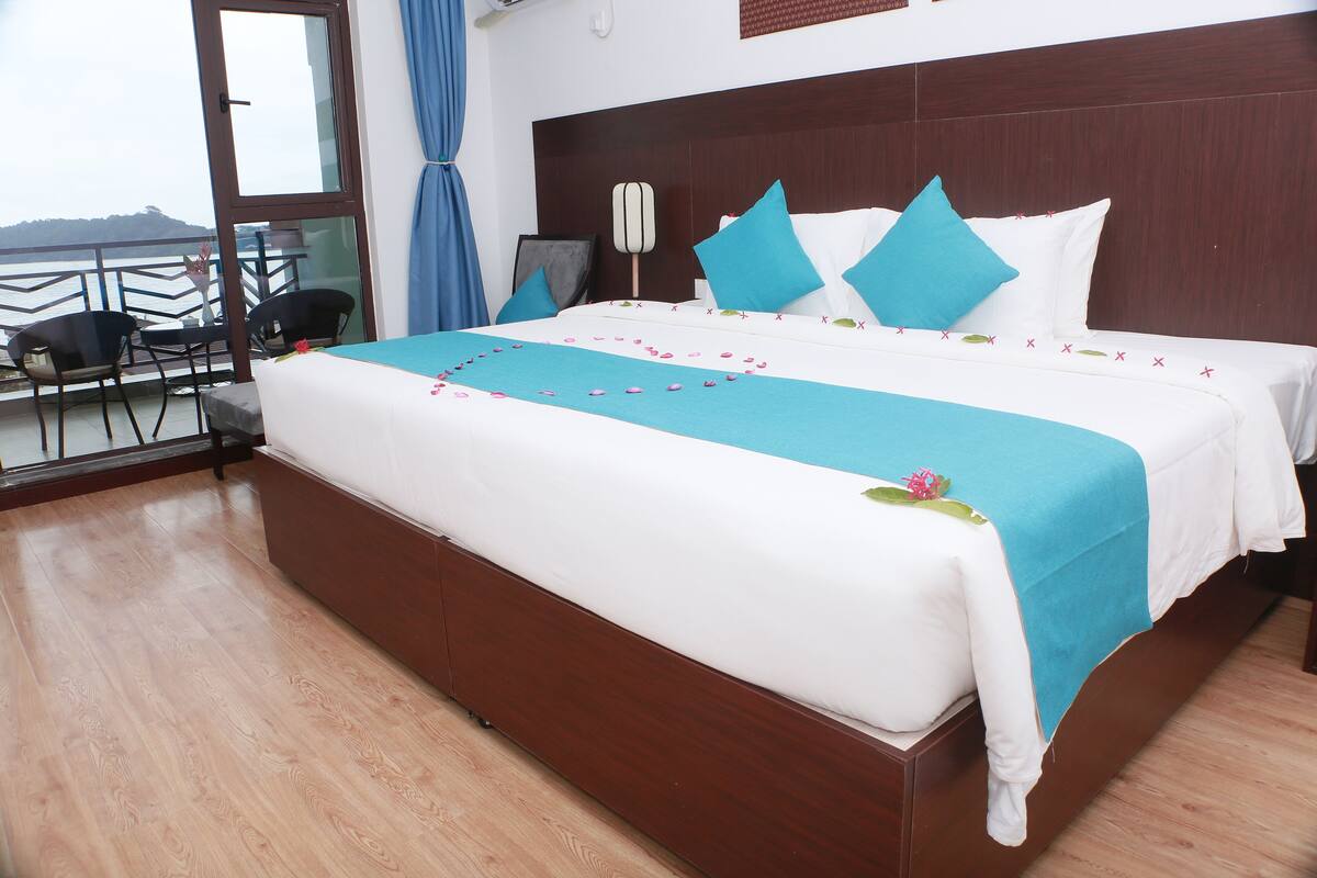 Ein Hotelzimmer mit einem großen Bett, einem Balkon mit Stühlen und Blick aufs Meer.