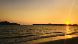 A sunset over a calm sea with gentle waves, a distant shoreline, and a boat in the water. - Sealong Bay ZhongQi Conifer Hotel (Prey Nob)
