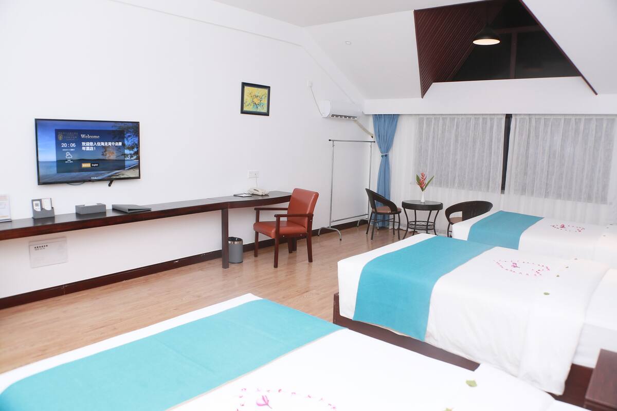 Ein Hotelzimmer mit zwei Betten, einem Schreibtisch, einem Stuhl, einem Fernseher und einem Fenster mit Vorhängen.