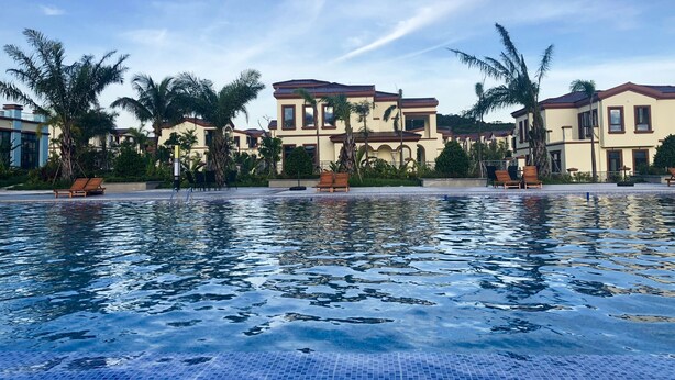 A swimming pool with lounge chairs and palm trees, surrounded by buildings with a Mediterranean architectural style. - Sealong Bay ZhongQi Conifer Hotel (Prey Nob)