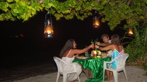 A table set up on a sandy beach with hanging lanterns above, surrounded by greenery. - Kuri Beach View Inn (Omadhoo)