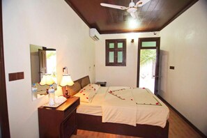 Une chambre d’hôtel équipée d’un lit, d’une table de chevet, d’une lampe, d’un miroir et d’un ventilateur de plafond.