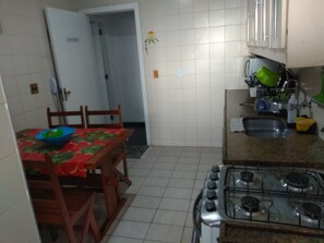 Uma cozinha com fogão a gás, pia e mesa de jantar com cadeiras.
