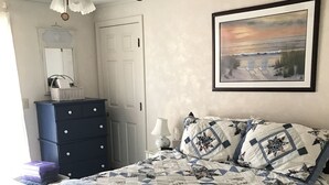 Un dormitorio con cama, cómoda, ventilador de techo, un cuadro en la pared y una puerta.