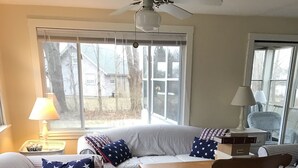 Una sala de estar acogedora con sofás a rayas, un sillón de balancín de madera, un tapete estampado y un ventanal con vistas al exterior.