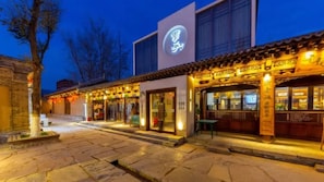 A traditional building with a modern entrance, stone pavement, and illuminated signage.