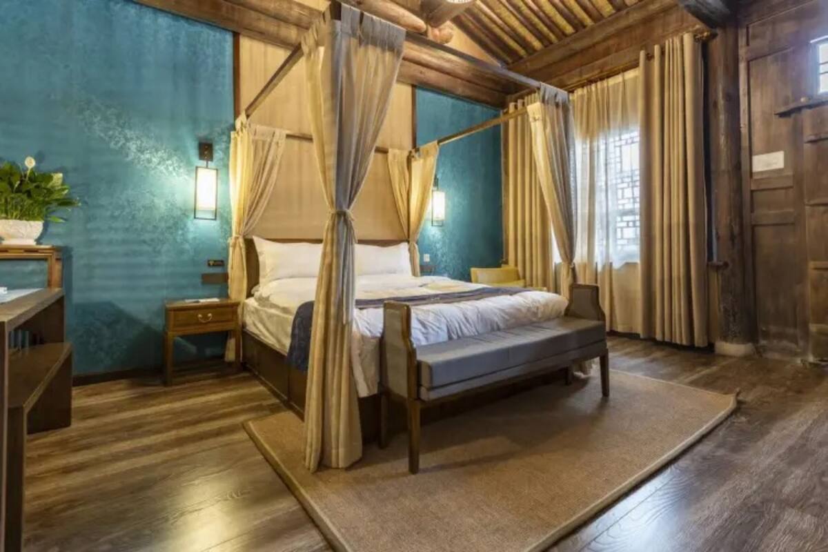 A four-poster bed with curtains, a bedside table, a nightstand, and a potted plant.