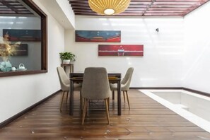 A dining area with a wooden floor, a table with four chairs, and two wall-mounted paintings.