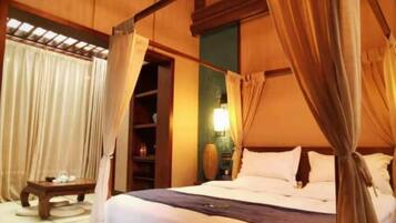 A bedroom with a canopy bed, a bedside table, a bench, and a nightstand with a lamp.