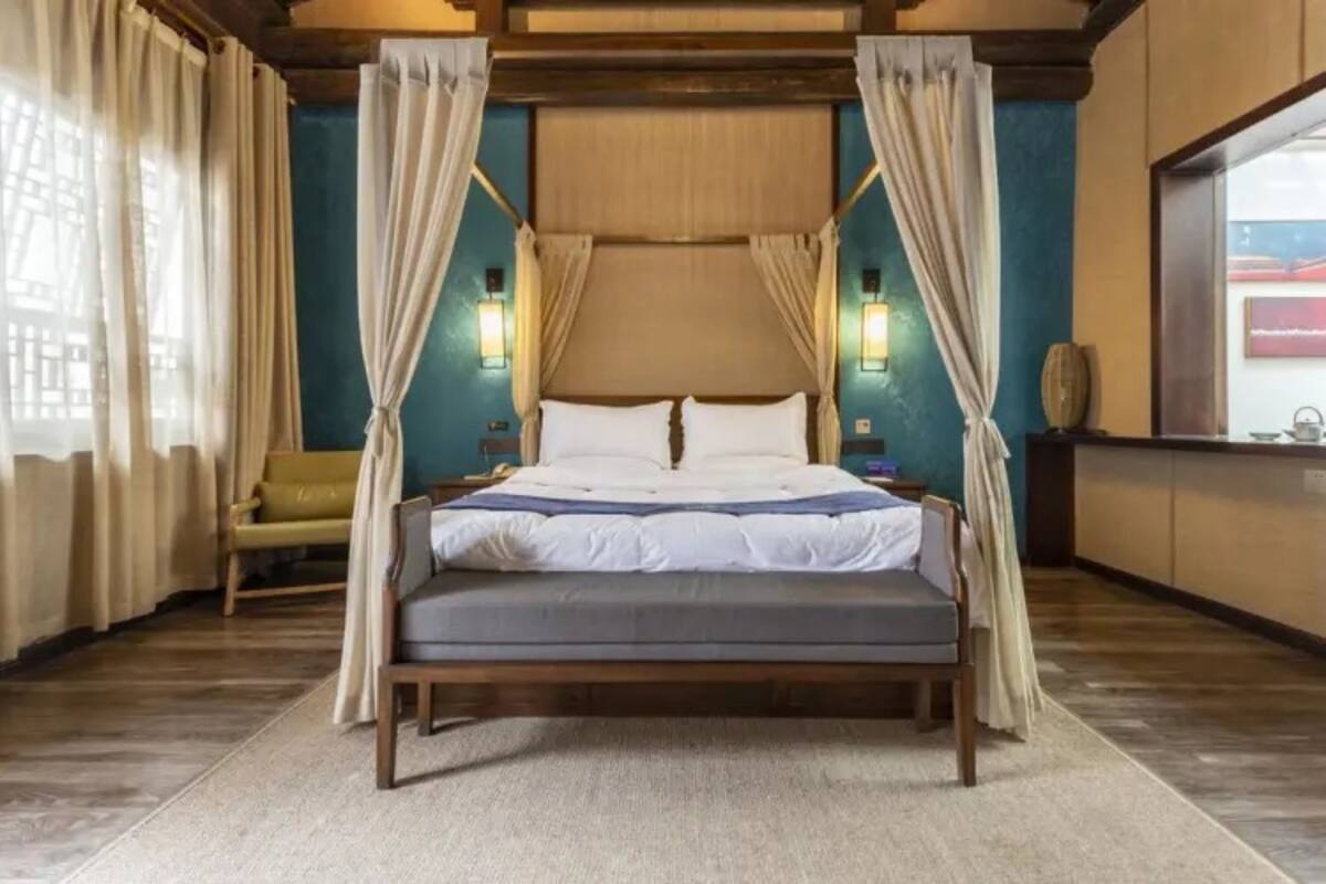 A bed with a canopy, a nightstand, a lamp, and a view of the outside.