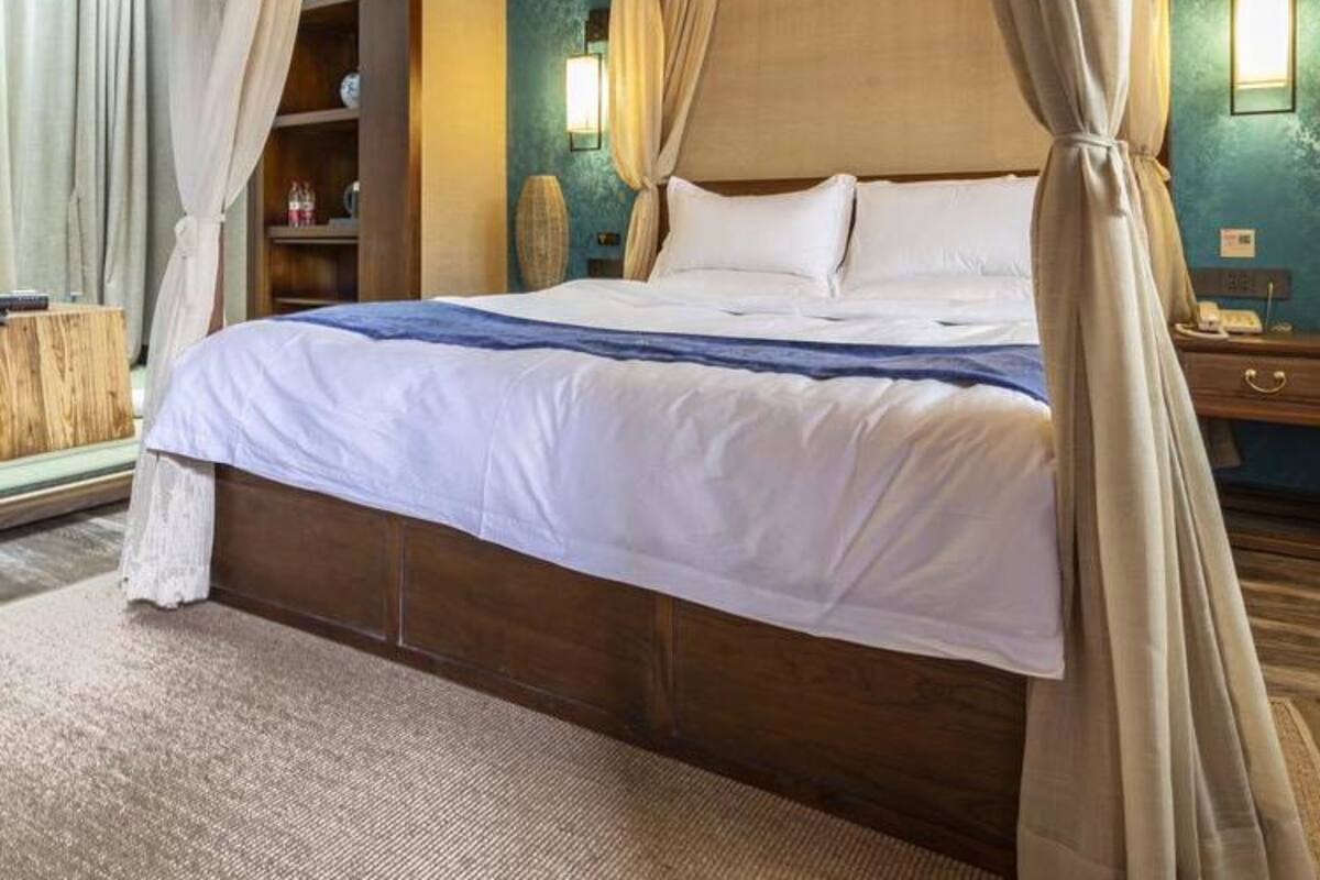 A four-poster bed with white linens, a wooden headboard, and beige curtains.