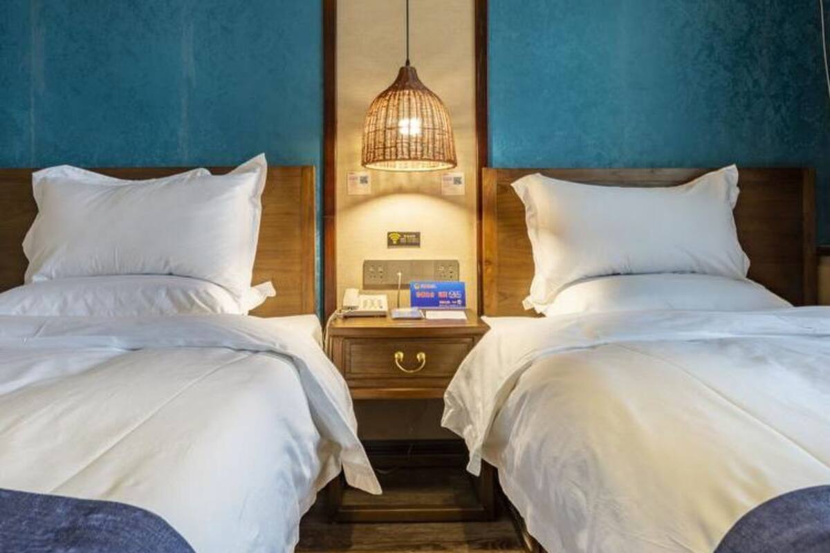 A hotel room with two beds, a nightstand with a lamp, and a wall-mounted control panel.