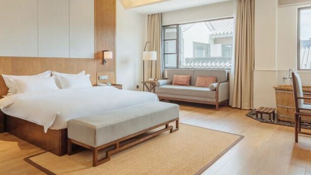 Una habitación de hotel moderna con una cama grande, un sofá, un escritorio y una ventana con cortinas.