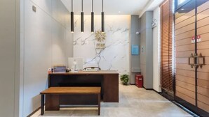 Un mostrador de recepción con pared de mármol, banco de madera y lámparas colgantes.