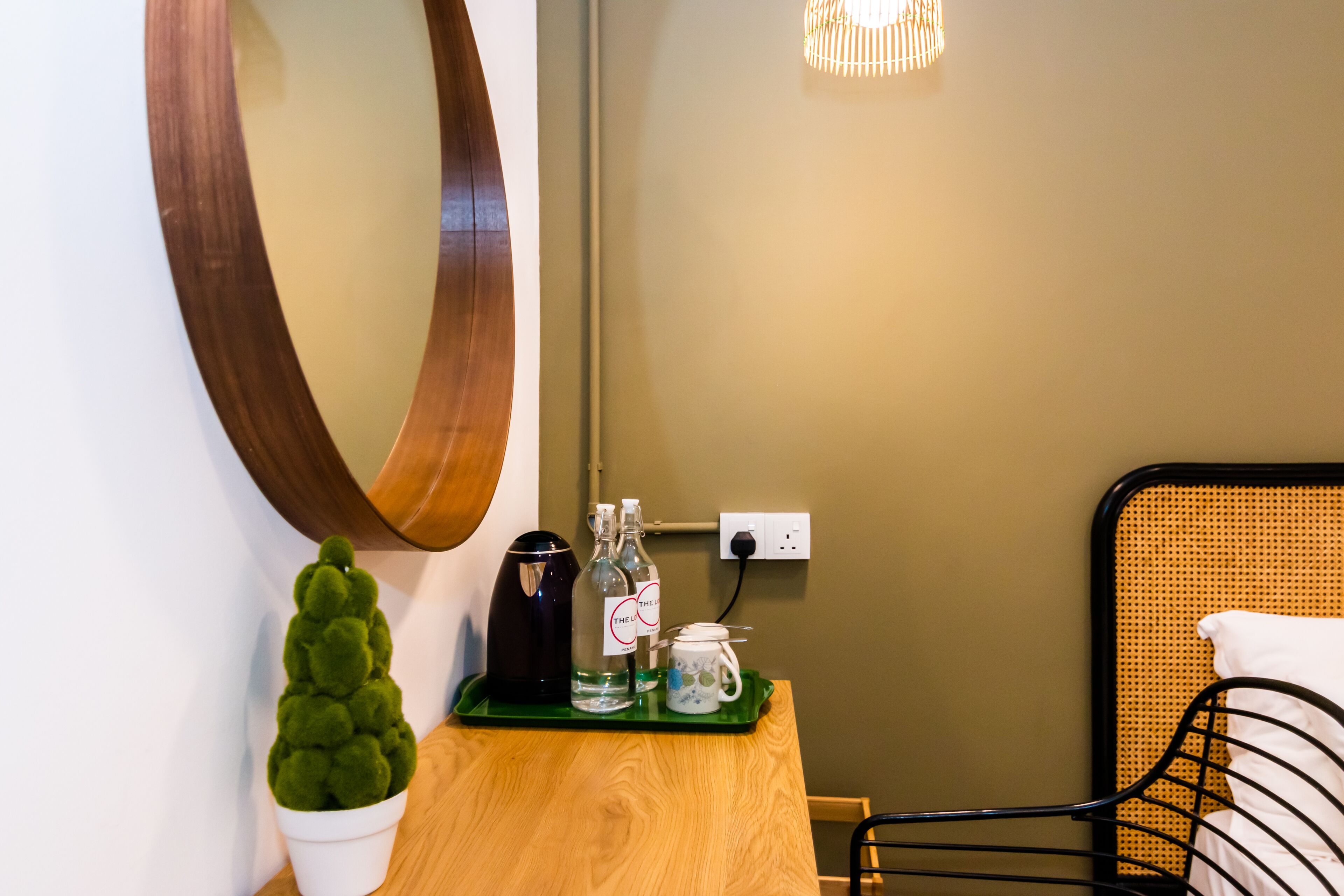 A wooden table with a green tray holding a small potted plant, a kettle, and a mug. A large mirror hangs on the wall above the table.