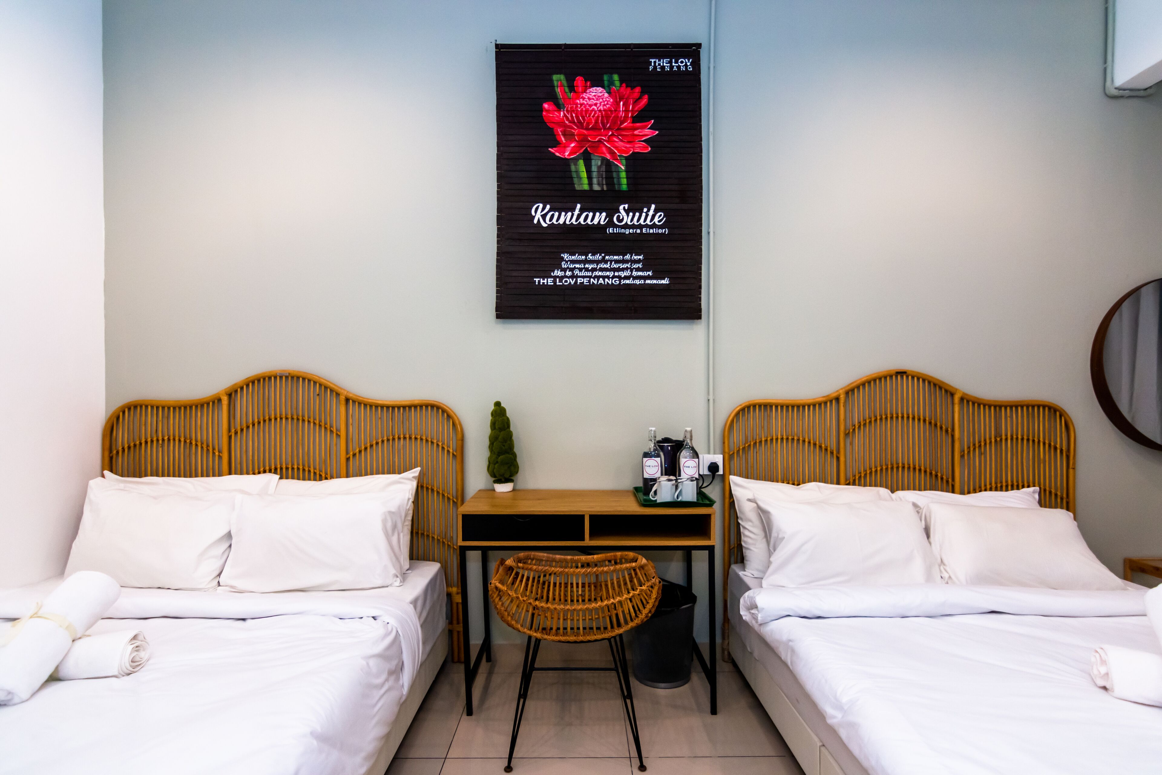 Una habitación de hotel con dos camas, una mesita pequeña con una silla y un cartel en la pared.