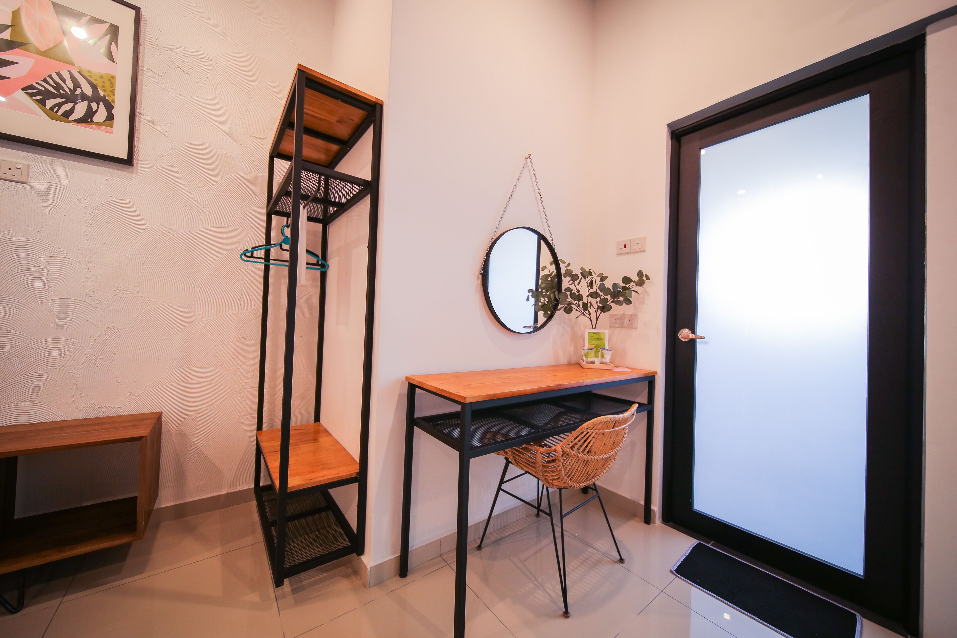 A modern interior with a wooden desk, a wicker chair, a tall black shelving unit, and a large mirror on the wall.