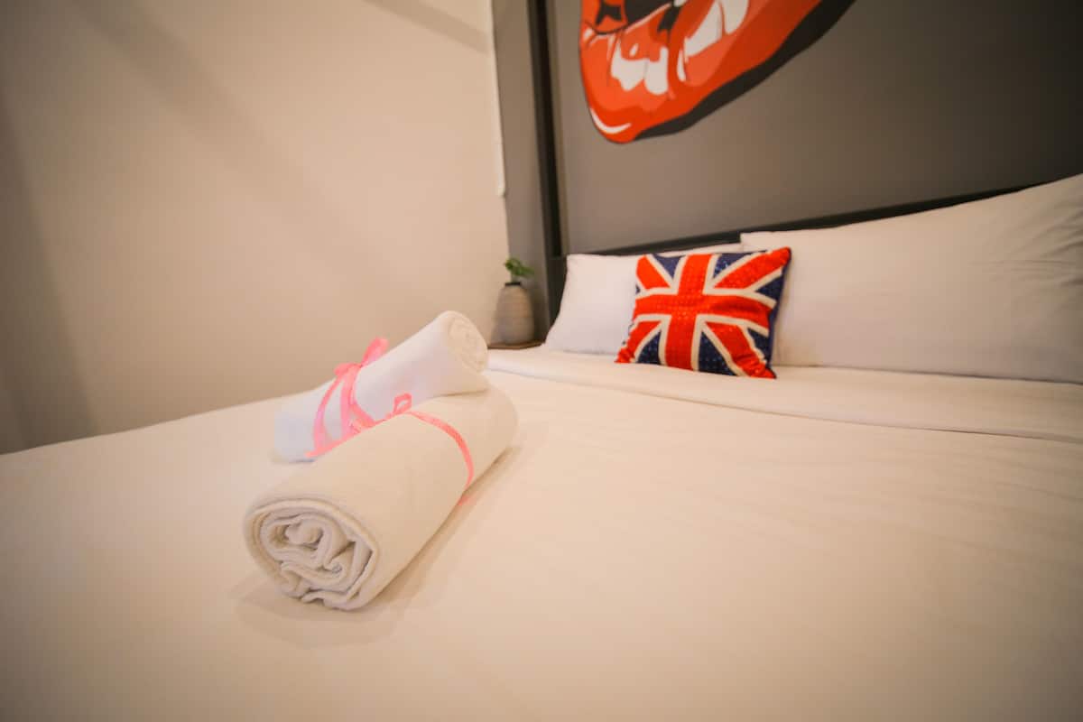 A neatly made bed with a rolled white towel and a pillow with a Union Jack design.