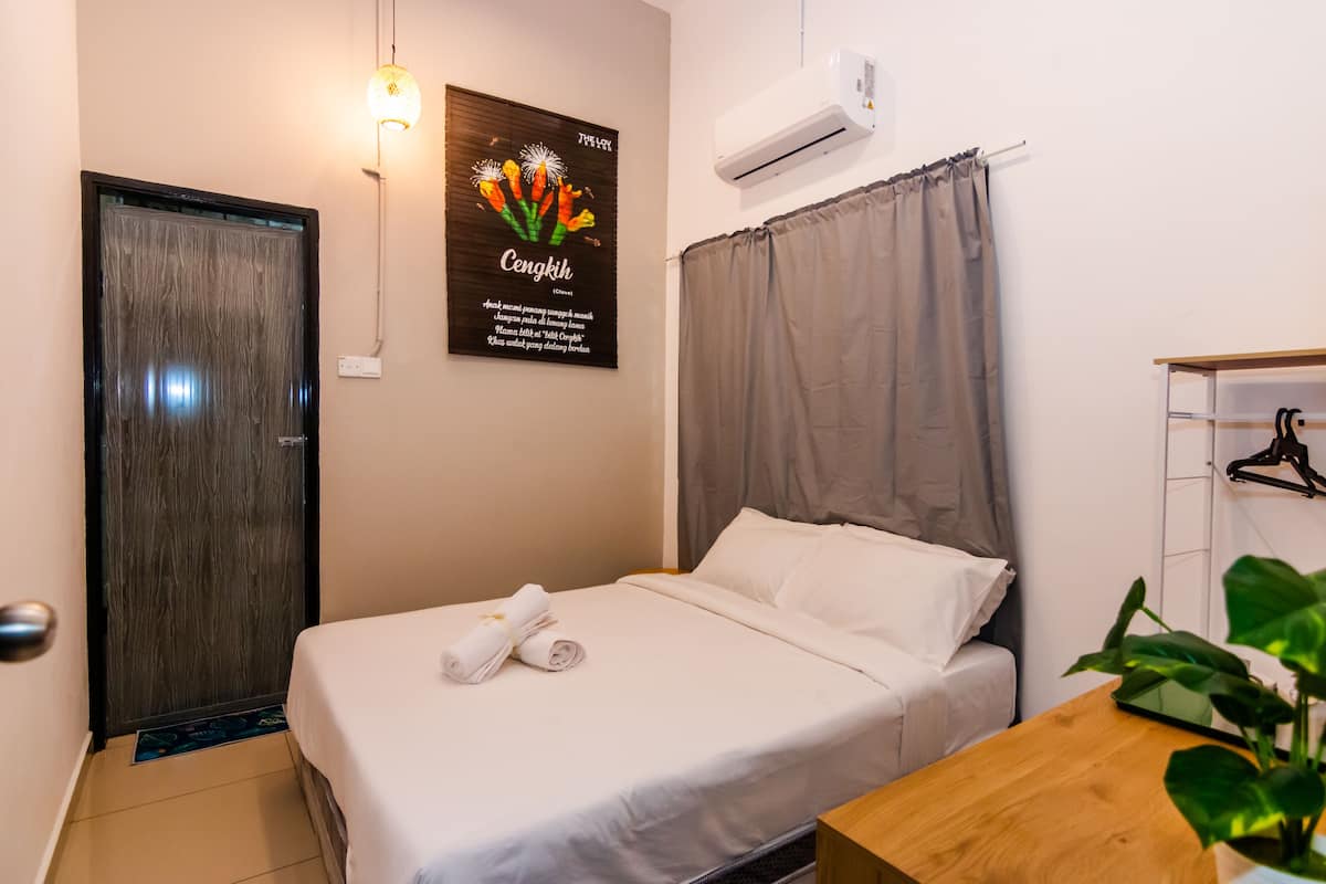 A neatly made bed with white linens and a rolled towel, a wooden nightstand, a wall-mounted air conditioner, and a poster with text and flowers.