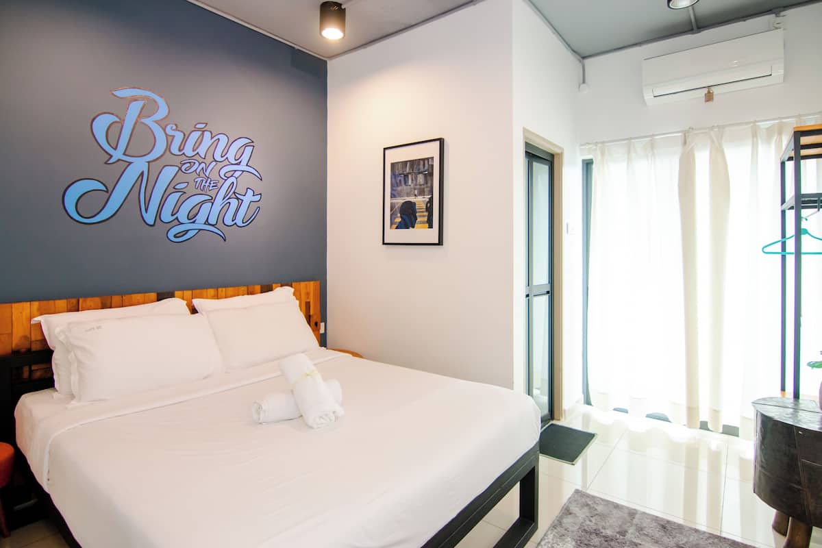 A neatly made bed with white linens and a towel, a wall sign reading "Bring on the Night", and a framed picture on the wall.