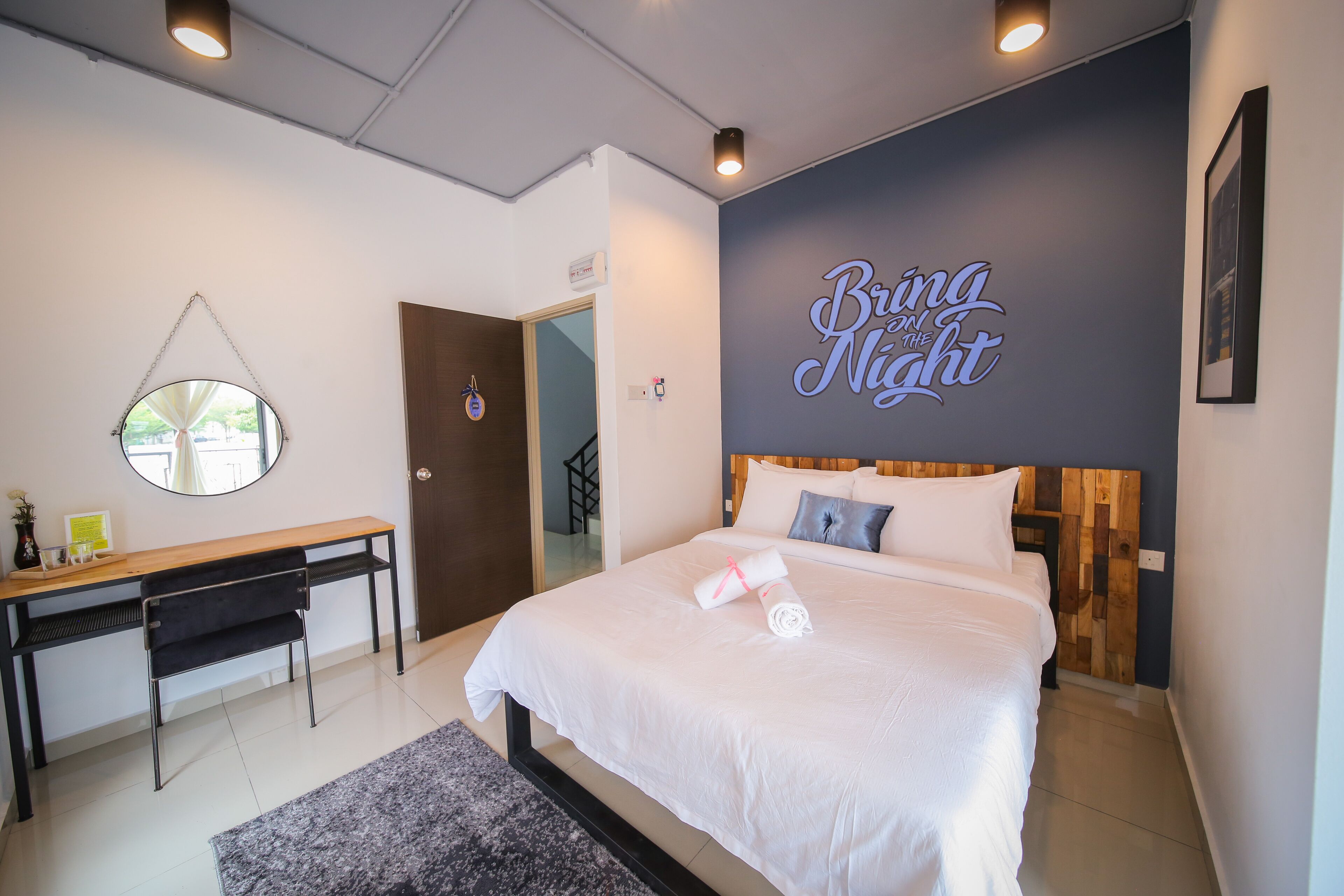 Une chambre d’hôtel moderne, équipée d’un lit, d’un bureau et d’un mur orné d’une inscription qui dit : « Que la nuit commence ».