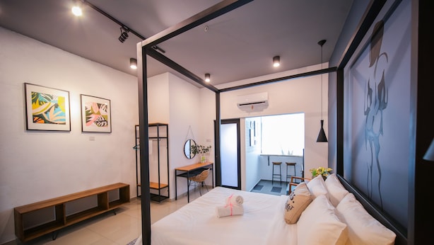 A modern hotel room with a bed, a desk, and a bench. There are two framed artworks on the wall and an air conditioning unit above the desk. - The Lov Penang (George Town)