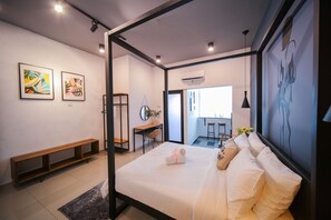Une chambre d’hôtel moderne avec un lit, un bureau et un banc. Deux œuvres d’art encadrées ornent le mur, et un appareil de climatisation est installé au-dessus du bureau.