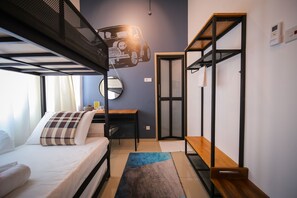 Habitación pequeña con literas, escritorio, silla, mesita, estante y puerta.