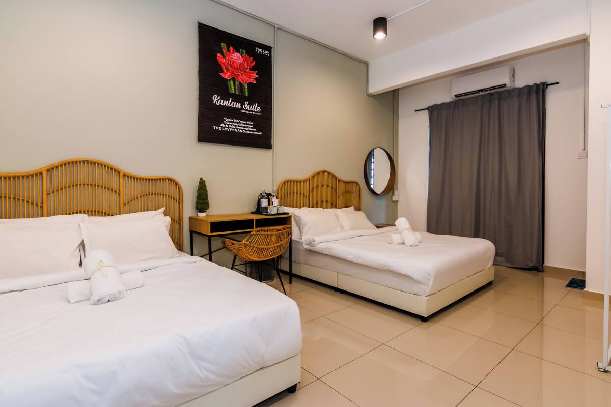 A hotel room with two beds, a small table with a bottle, a chair, a mirror, and a curtain.