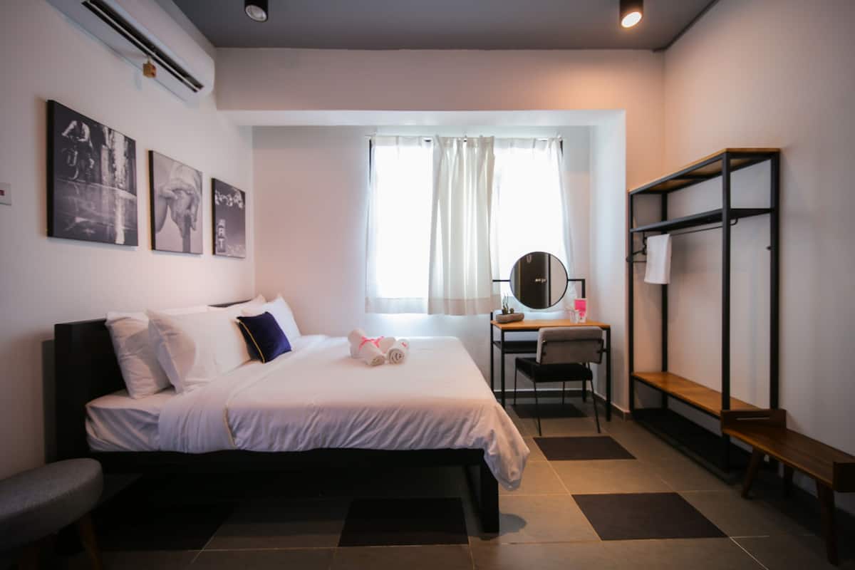 A hotel room with a bed, desk, chair, and a bench.