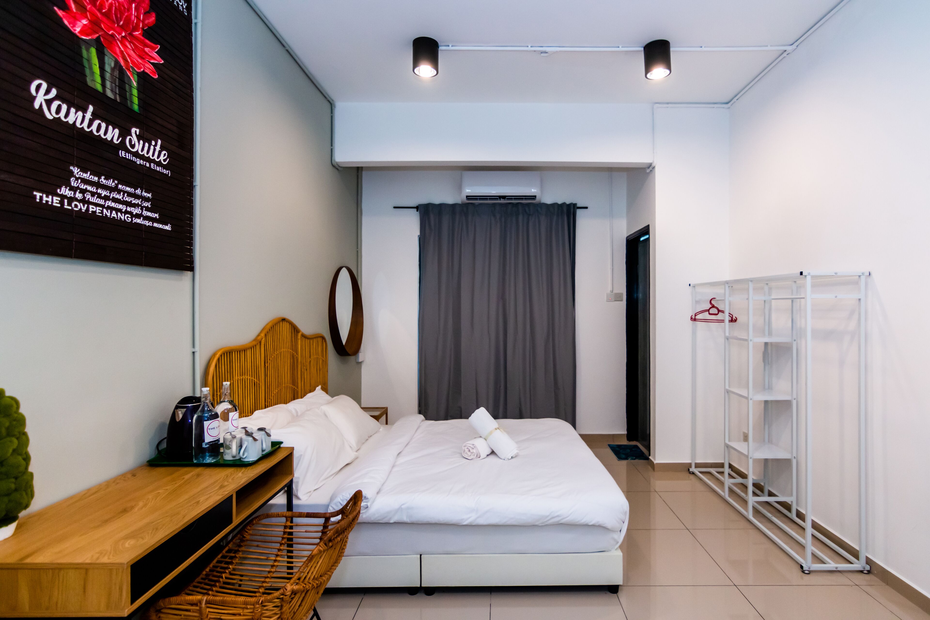 A hotel room with a bed, a wooden bench, a small table with toiletries, a wardrobe, and an air conditioning unit.
