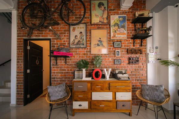A room with a brick wall, a wooden cabinet with drawers, wicker chairs, and a door. - The Lov Penang (George Town)