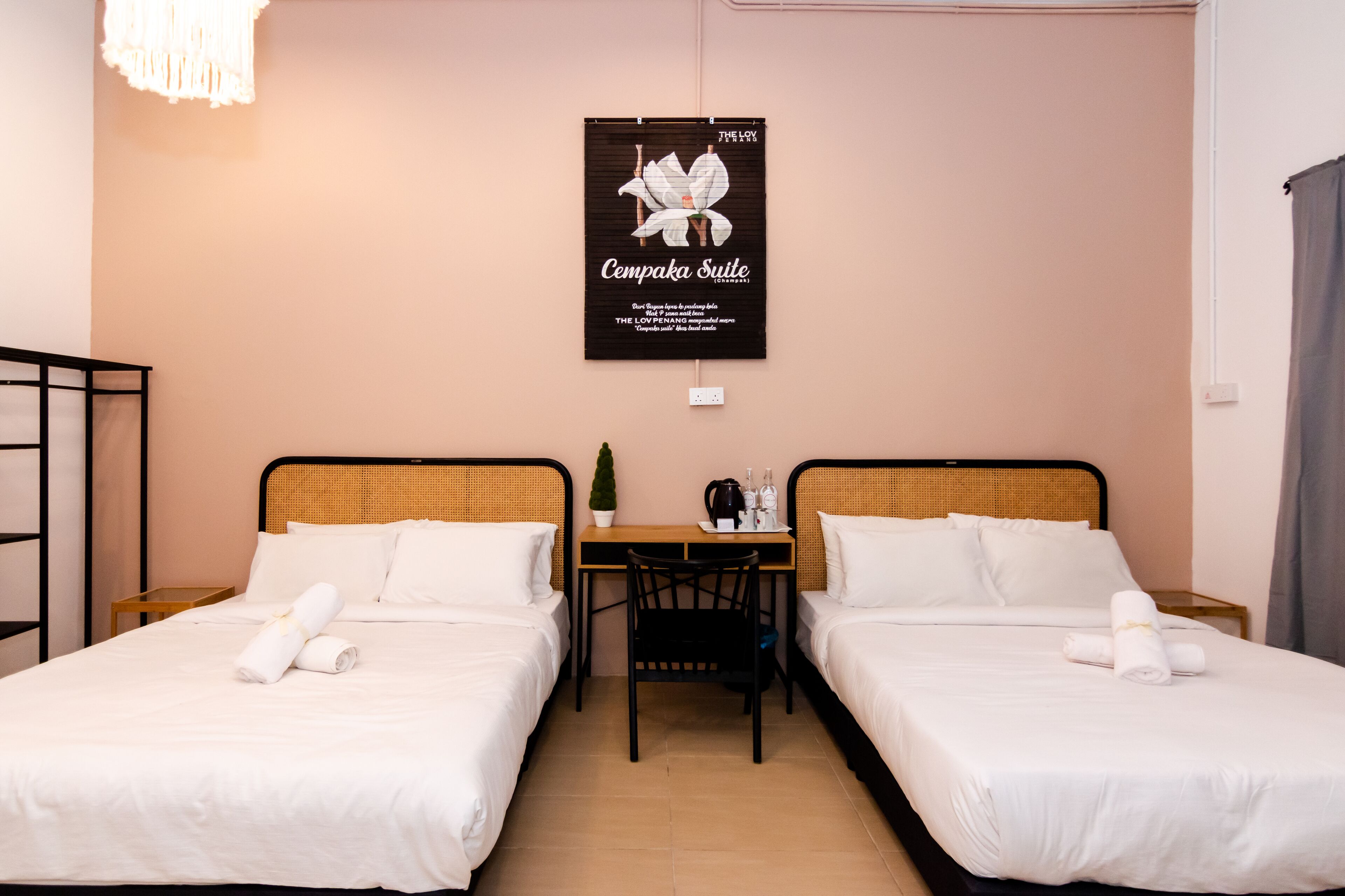 A hotel room with two beds, a small table, a chair, and a poster on the wall.