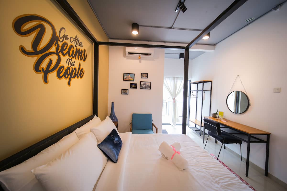 A hotel room with a bed, a desk, a chair, and a motivational quote on the wall.