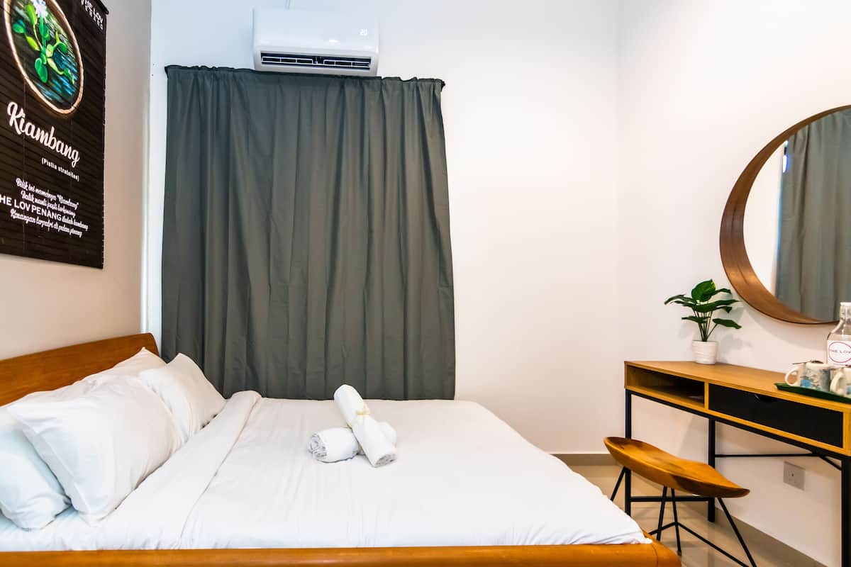 A hotel room with a bed, a desk, a mirror, and a potted plant.