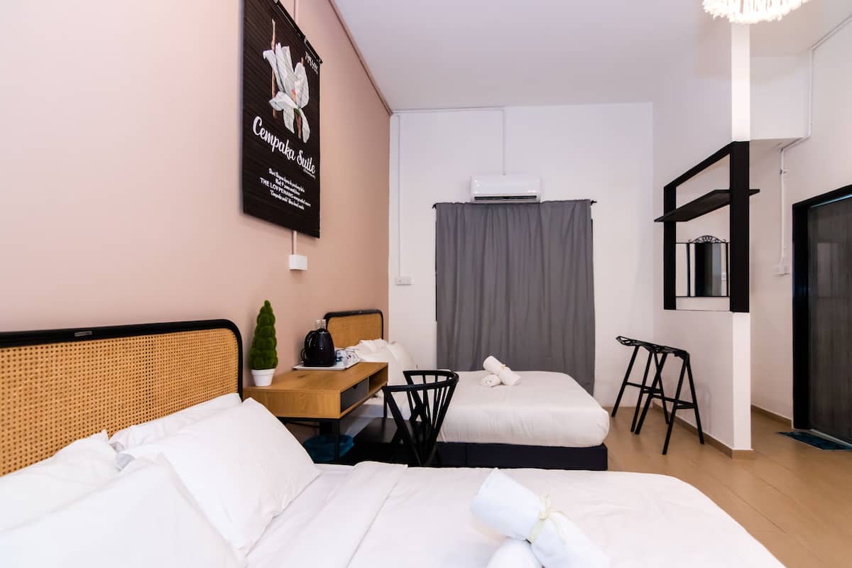 A hotel room with two beds, a small table with a plant, a wall-mounted air conditioner, and a mirror above the bed.