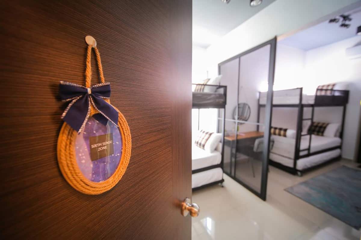 A room with bunk beds, a glass partition, and a door with a woven bag hanging on it.