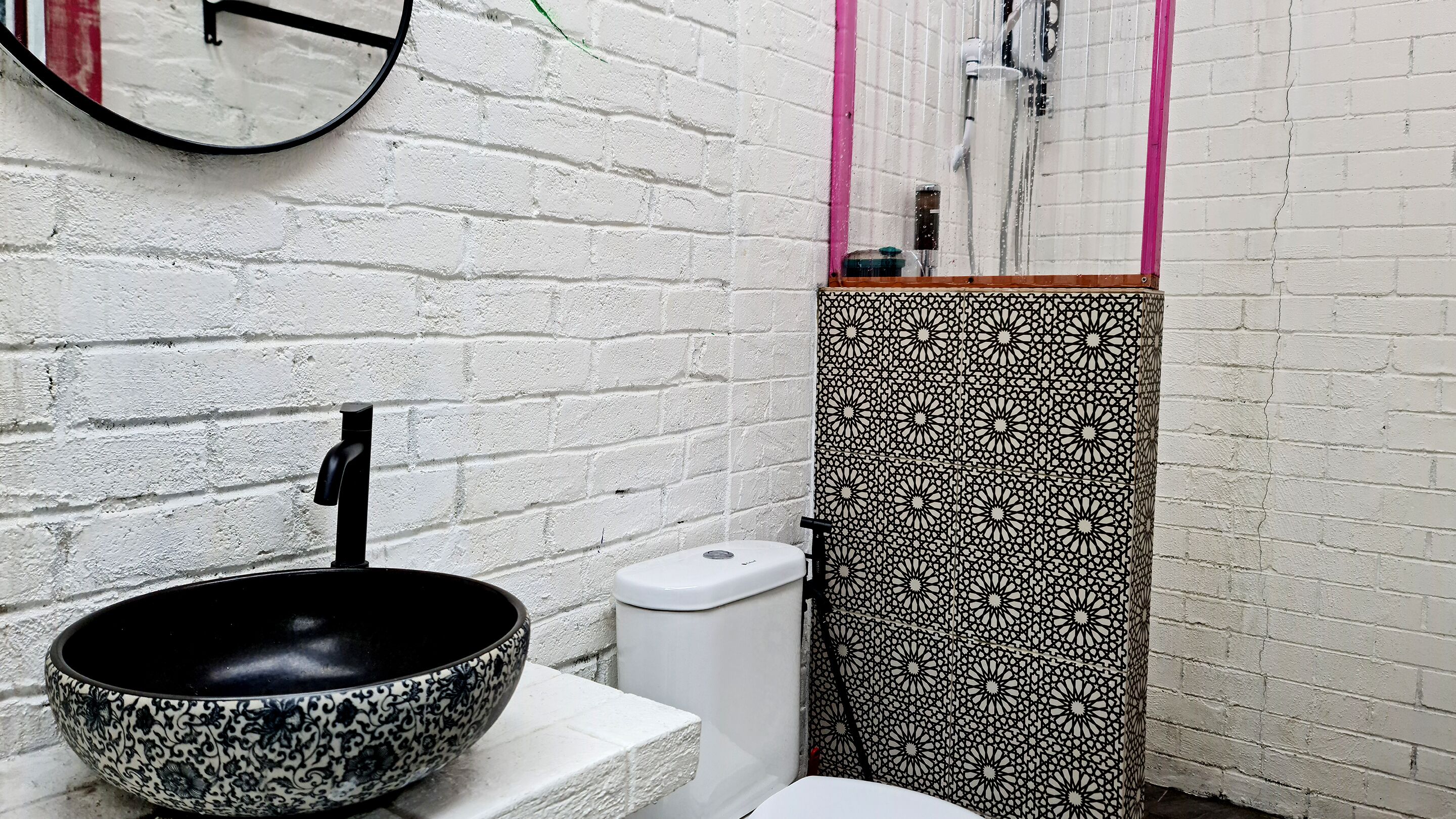 Un bagno con un lavabo a forma di ciotola con motivo bianco e nero, un water bianco e uno specchio con cornice rosa.