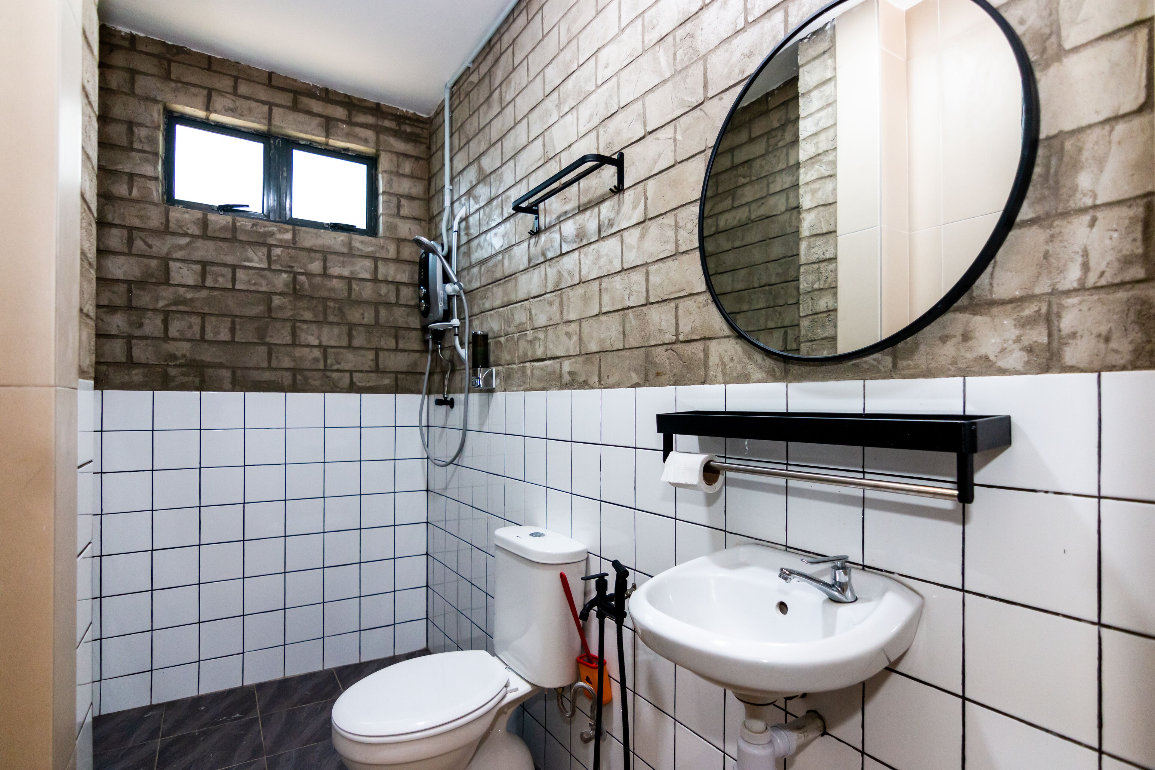 Een badkamer met toilet, wastafel en douche. Er is een raam boven het toilet en een spiegel boven de wastafel.