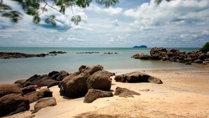 A beach with large rocks in the foreground and a calm sea in the background. - The Lov Penang (George Town)