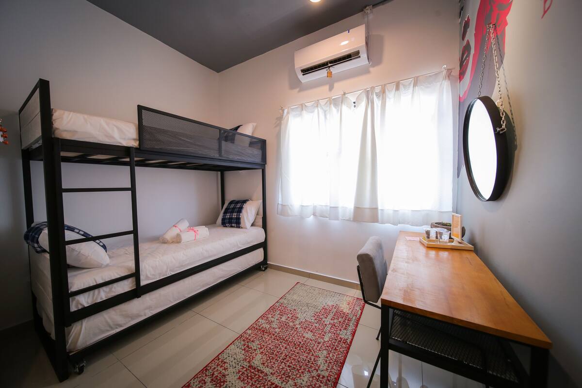 A bunk bed room with a desk and chair, an air conditioner, and a window with curtains.