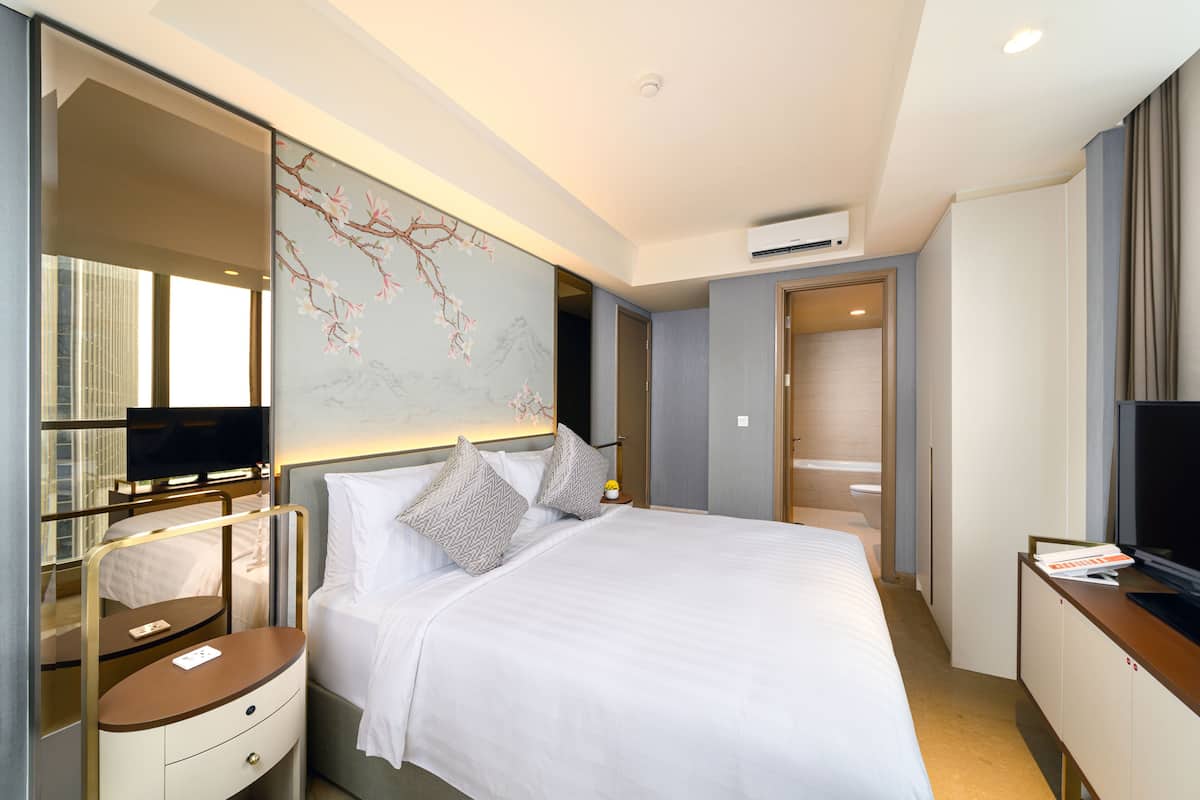 A modern hotel room with a large bed, a bedside table, a TV, and a wall-mounted artwork.