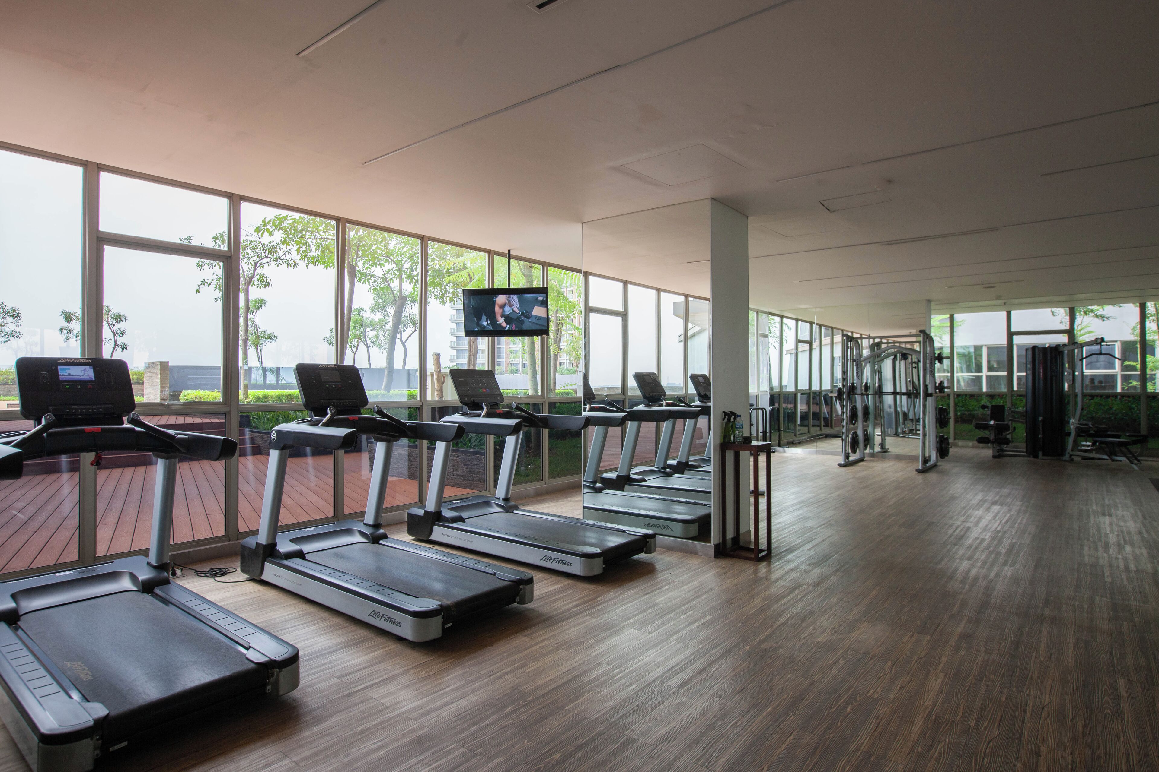 Ein Fitnessstudio mit Laufbändern, Kraftgeräten und einem Fernsehbildschirm.