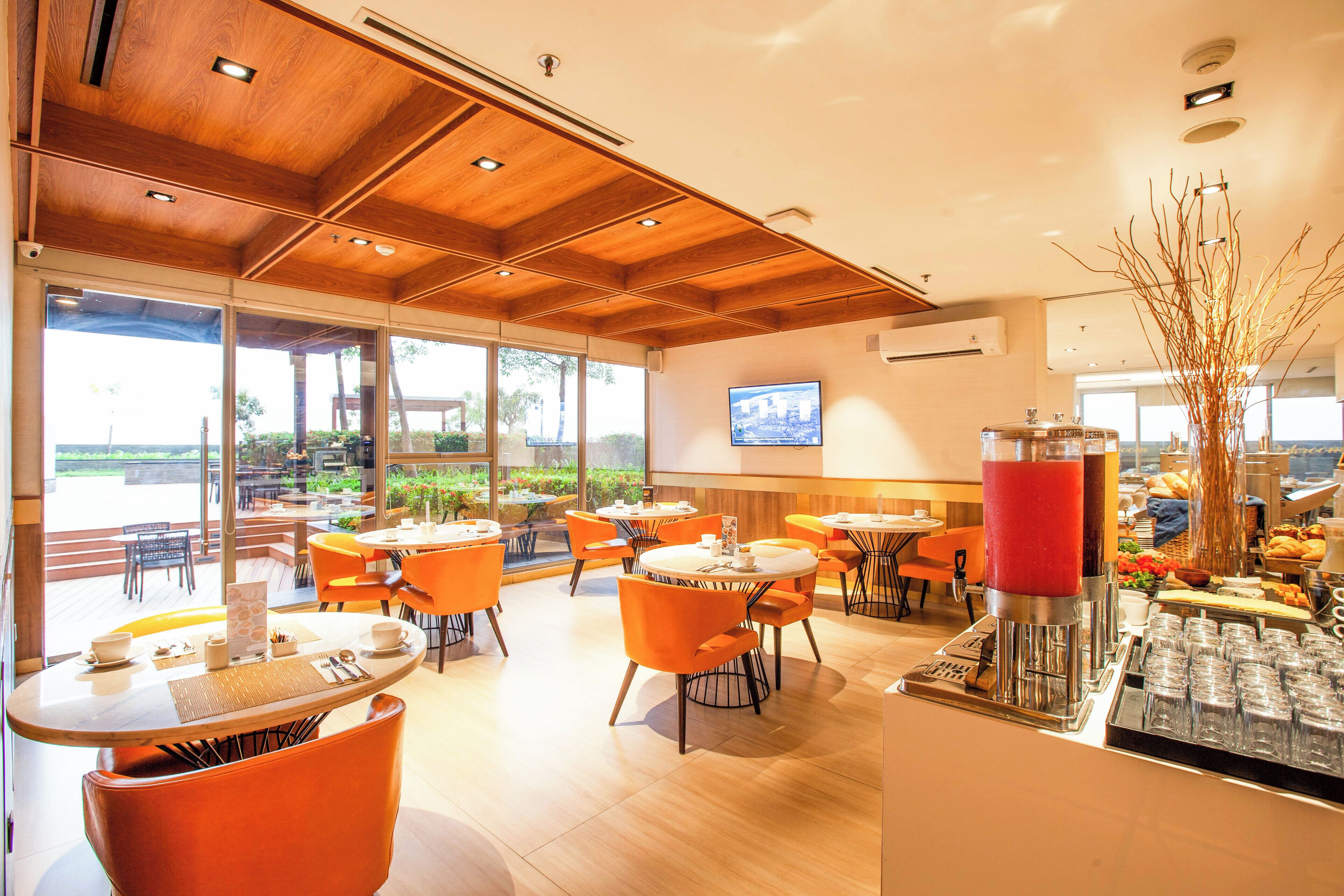 Un restaurant moderne avec des poutres en bois au plafond, des chaises orange et un espace buffet proposant une variété de plats.