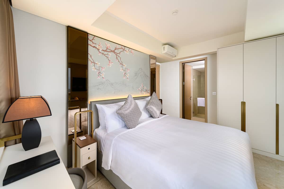 A hotel room with a bed, bedside table, lamp, and a large mirror.