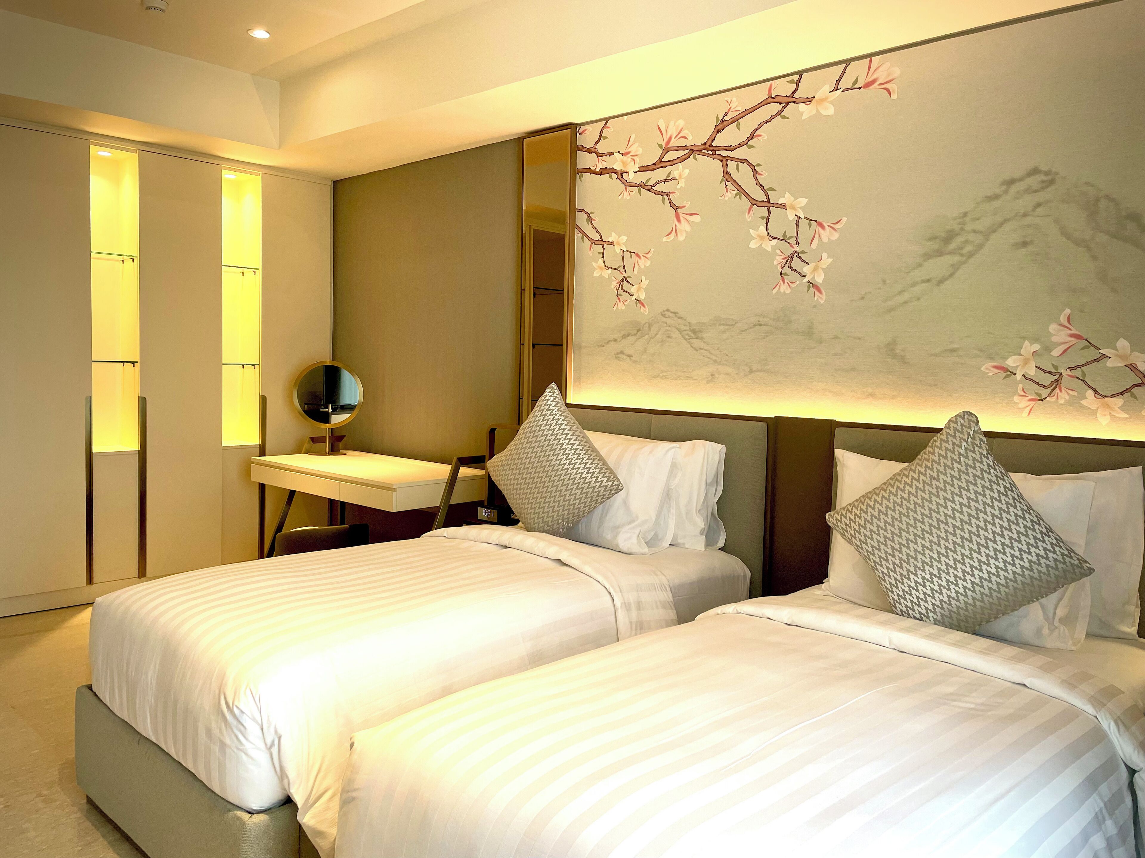 Une chambre d’hôtel avec deux lits, un bureau avec un miroir et un mur orné d’une fresque florale.