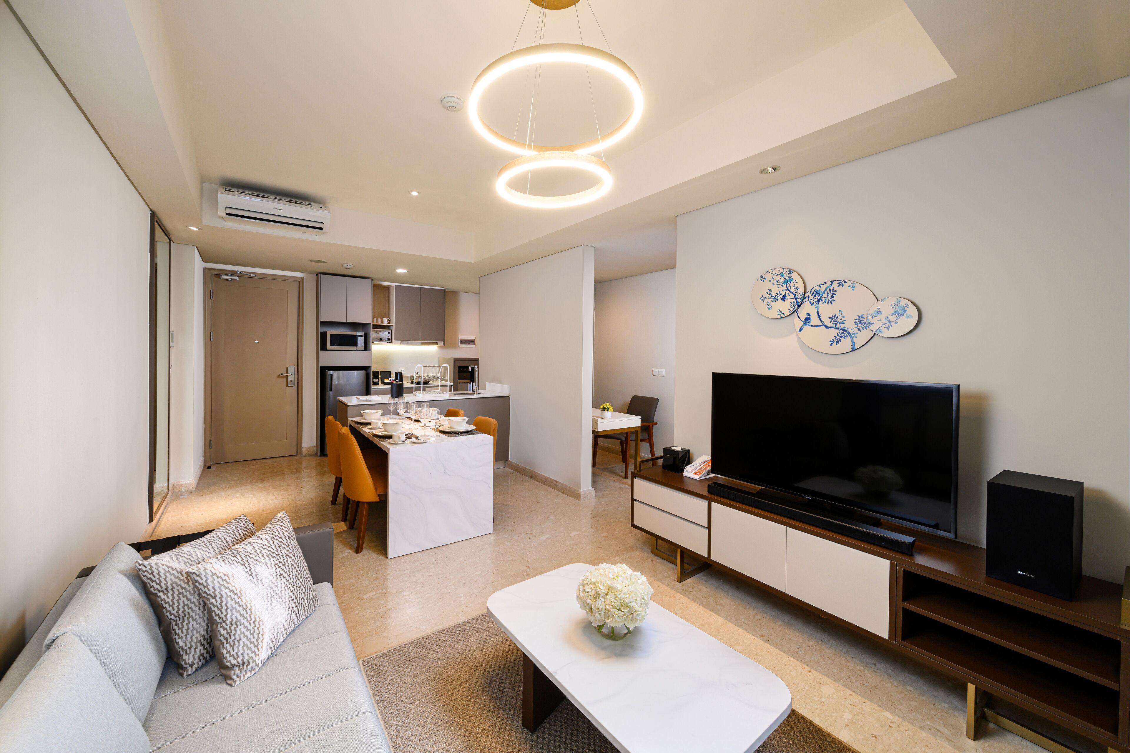 A modern living room with a sofa, coffee table, TV, and a dining area in the background.